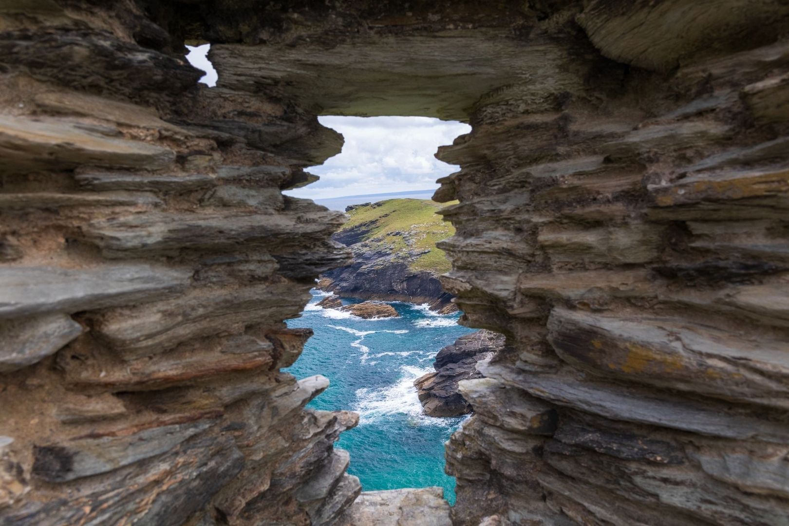 Layered sea cliffs frame turquoise water and a grassy coastal headland