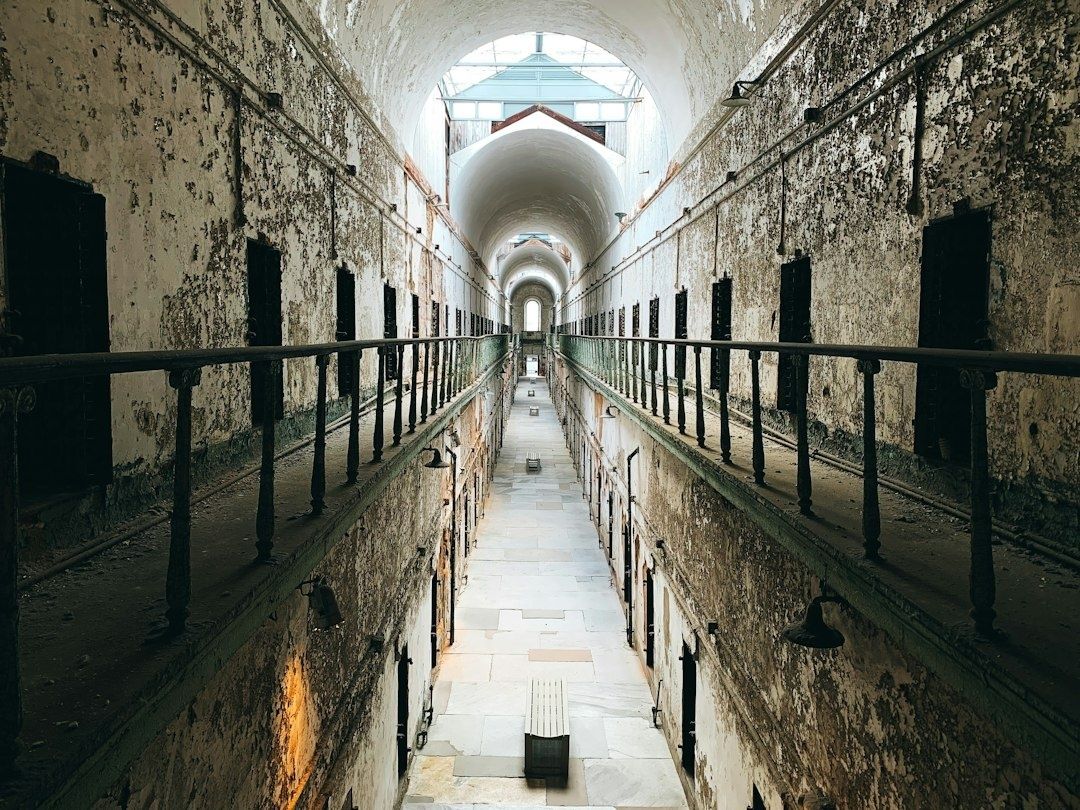 Weathered prison corridor with rows of dark cell doors and arched ceilings